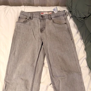 Levi's 501 ljusgrå jeans - Säljer ett par klassiska Levi's 501 jeans i ljusgrå tvätt. Jeansen har rak passform, fem fickor och knappgylf. Perfekta för dig som gillar en tidlös och avslappnad stil. Levi's patch bak i midjan och ikoniska sömmar på bakfickorna.