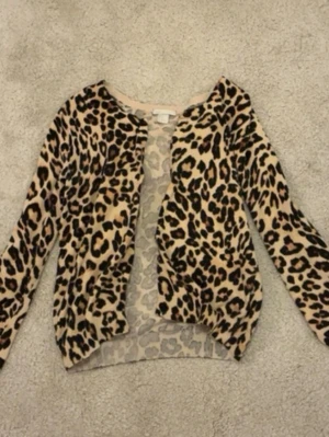 Leopardmönstrad kofta från H&M - Säljer en snygg leopardmönstrad kofta från H&M. Koftan har långa ärmar och är i mjukt, stretchigt material. Beige botten med bruna och svarta fläckar ger en trendig look. Perfekt för dig som vill sticka ut lite extra.