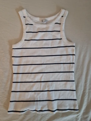 Vit ribbat linne - Säljer ett vitt ribbat linne från Cubus i storlek XS. Linnet har svarta horisontella ränder och breda axelband. Materialet är stretchigt och mjukt, perfekt för en avslappnad och stilren look. Passar till jeans, kjol eller shorts. Aldrig använt men Lapparna saknas. Hund finns I hemmet. 