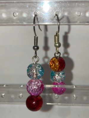 Färgglada pärlörhängen med krokar - Handgjorda unika örhängen med tre runda pärlor i olika färger: röd, rosa, blå och gul. Pärlorna har en krackelerad effekt som ger extra lyster. Metallkrokar i silverfärg. Perfekta för dig som gillar färg och vill sticka ut. Kontakta mig om du vill köpa eller har frågor.