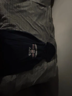 Mörkblå hoodie Vinson Original - Mörkblå hoodie från Vinson Original med tryck på bröstet i vitt och rött. Klassisk modell med huva och ribbade muddar. Perfekt för en avslappnad och sportig stil. Materialet känns mjukt och bekvämt mot huden.