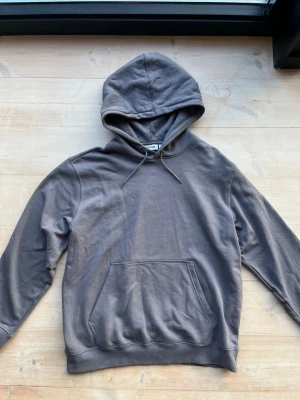 Mörkgrå hoodie från Weekday strl L - Snygg grå hoodie från Weekday med klassisk känguruficka och dragsko i huvan. Tillverkad i mjuk bomullsmix som känns skön mot huden. Perfekt för en avslappnad och stilren look.