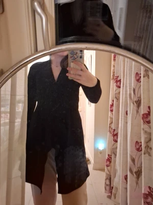 Svart lång kofta med V-ringning - Säljer en svart lång kofta med V-ringning och långa ärmar. Koftan har en rak passform och går ner över höfterna. Perfekt att slänga över en topp eller t-shirt för en enkel och stilren look.