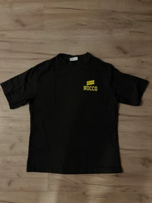 EXTREMT SÄLLSYNT Svart NOCCO t-shirt  - Svart NOCCO-t-shirt i mjuk bomull med gul logga på bröstet och stort “TIME TO FOCUS”-tryck på ryggen. Extremt sällsynt modell som producerats i mycket begränsat antal – finns endast ett fåtal exemplar. Ett unikt plagg för samlare och NOCCO-fans. BUDGIVNING AKTIV, PRIS GÅR ATT DISKUTERA