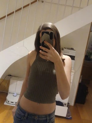 Ribbat grönt linne - Snygg ribbad linnetopp i mörkgrönt med croppad passform och ärmlös design. Perfekt till jeans eller kjol för en chill look. Toppen har en hög halsringning och är tillverkad i ett stretchigt material. 💕💕