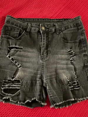 Svarta slitna jeansshorts S - Svarta jeansshorts med slitna detaljer och fransig kant. Klassisk femficksmodell med knapp och dragkedja framtill. Perfekta för en avslappnad stil.