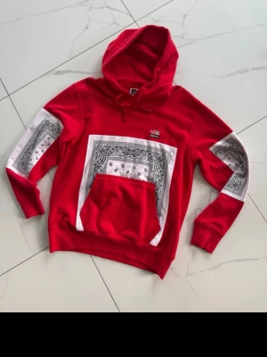 Röd Supreme x TNF hoodie sweatshirt SIZE-S - Säljer en röd hoodie från Supreme x The North Face med feta bandanamönster i vitt och svart på bröstet och ärmarna. Klassisk huva med dragsko och stor magficka. Perfekt statement-plagg för dig som vill sticka ut. Mjuk bomullskvalitet.