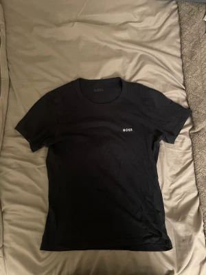 Svart t-shirt från BOSS - Svart t-shirt från BOSS med klassisk passform och rund halsringning. Diskret BOSS-logga broderad på bröstet. Perfekt basplagg i mjuk bomull som funkar till allt.