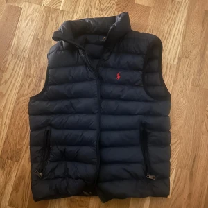 Svart dunväst från Polo Ralph Lauren - Svart dunväst från Polo Ralph Lauren med röd broderad logga på bröstet. Nypris 3300 knappt använd 
