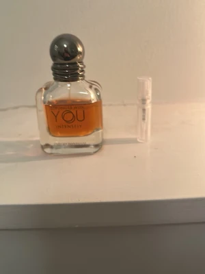 Armani Stronger With You Intensely - Säljer en parfymflaska av Armani Stronger With You Intensely. Flaskan är genomskinlig med rundade kanter och har en silverfärgad, rund kork. Parfymen har en bärnstensfärgad vätska och flaskan är i glas. En liten provflaska medföljer.