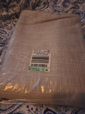 Beige gardin - Beige gardin i tunt, lätt tyg från Jotex.Gardinen har ett diskret rutmönster och levereras i originalförpackning. Perfekt för att släppa in ljus men ändå ge lite insynsskydd. Passar bra till de flesta inredningsstilar.