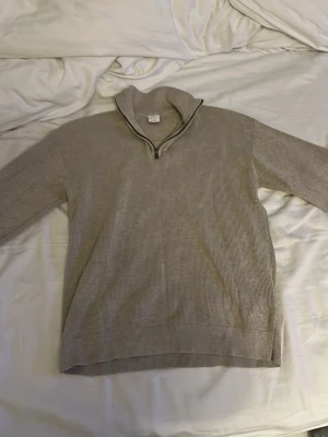 Beige stickad tröja med halvzip Lindex - Beige stickad tröja från Lindex med halvzip och hög krage. Tröjan har ribbstickad struktur och långa ärmar, perfekt för lager på lager. Enkel och stilren design som passar till det mesta.