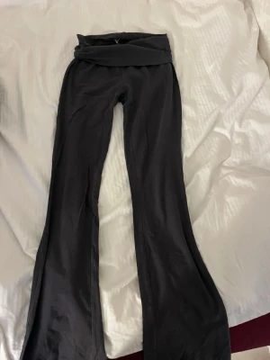 Svarta bootcut leggings med omlottmidja - Säljer ett par svarta leggings med bootcut-ben och omlottmidja. De har en snygg, figurnära passform upptill och släpper ut nedtill för en trendig siluett. Perfekta till sneakers eller boots och superbekväma för vardagslooken.