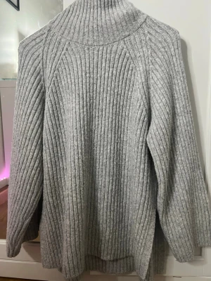 Ljusgrå polotröja i ribbstickat - Säljer en oversized ljusgrå polotröja i ribbstickat material. Tröjan har långa ärmar, hög polokrage och en avslappnad passform. Perfekt för kalla dagar och enkel att styla med jeans eller leggings.