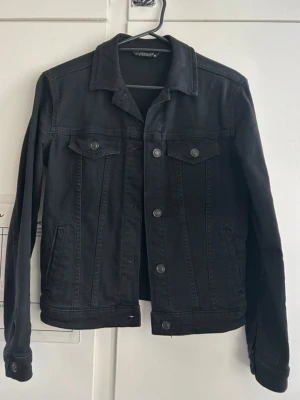 Svart jeansjacka – LCW Jeans - Snygg svart jeansjacka från LCW Jeans i storlek XS. Klassisk modell med knappar framtill och fickor både uppe och på sidorna. Passar perfekt till vardags, över en t-shirt eller hoodie.  ✅ Färg: Svart ✅ Storlek: XS ✅ Märke: LCW Jeans ✅ Skick: Mycket bra – använd några gånger men inga skador eller fläckar