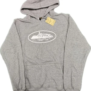 Grå Cortiez hoodie - Snygg grå hoodie med vit tryckt illustration framtill. Klassisk känguruficka och huva med dragsko. Perfekt för en avslappnad och cool stil. Mjuk bomullsblandning som känns skön mot huden.