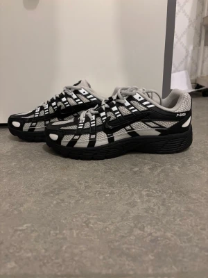 Nike P-6000 svartvita sneakers - Nike P-6000 sneakers i svart och vitt med sportig design och tydliga paneler. Ovandel i mesh och syntetmaterial med svarta detaljer och vit bas. Tjock svart sula och klassisk Swoosh-logga på sidan. Perfekta för en streetwear-look.