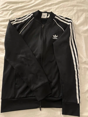 Svart Adidas track jacket och byxor  - Klassisk svart Adidas track sett. Skönt material som sitter bekvämt på kroppen. Använd några få gånger 