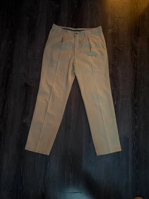Beige chinos från Hugo Boss Golf - Stilrena beige chinos från Hugo Boss Golf med klassisk rak passform och bälteshällor. Tillverkade i mjuk bomull som ger en skön känsla hela dagen. Perfekta för dig som gillar en clean och tidlös look.