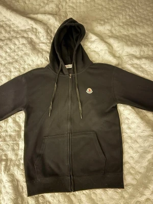 Svart zip hoodie från Moncler - Säljer en svart hoodie från Moncler med dragkedja framtill och två stora fickor. Klassisk huva med dragsko och Moncler-logga på bröstet. Tillverkad i mjukt bomullsmaterial som känns skönt mot huden. Perfekt för en avslappnad och stilren look. På sista bilden så ser ni hur den sitter på mig för referens. Jag är 194cm och väger 90kg. Som ni ser är det lite katthår på den, kommer givetvis tvätta och rulla bort hårstråna ifrån den innan den skickas iväg. 🙂