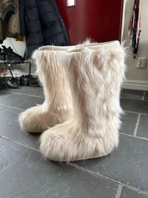 Beiga fluffiga moon boots - Supermysiga beiga moon boots med långhårigt fuskpälsmaterial. Bootsens insida är mjuk och vadderad för extra komfort. Perfekta för att sticka ut i vinter med sin unika och fluffiga look. Använda fåtal gånger.