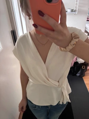 Söt tröja - Snygg vit omlottopp med knyt i sidan och v-ringad hals. Toppen har korta ärmar och ett mjukt, lätt tyg som ger en avslappnad men chic look. Perfekt att styla med jeans eller kjol för en trendig outfit.