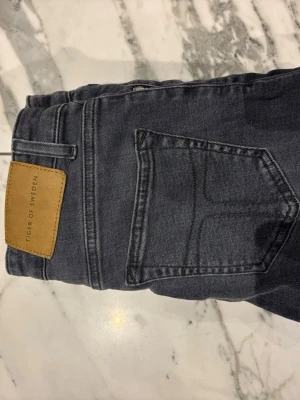 Grå skinny jeans Tiger of Sweden - Snygga grå skinny jeans från Tiger of Sweden med klassisk femficksdesign och läderpatch bak i midjan. Jeansen har smal passform och raka sömmar, perfekta till en trendig vardagslook.