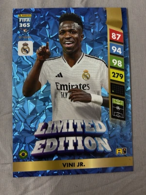 Panini FIFA 365 Limited Edition-kort - Samlarkort från Panini FIFA 365-serien, Limited Edition med Vini Jr. från Real Madrid. Kortet har en glansig blå bakgrund, spelarens statistik och klubbmärke. Perfekt för fotbollsentusiaster och samlare av trading cards. Kortet är även XL storlek. Köpare står för frakt