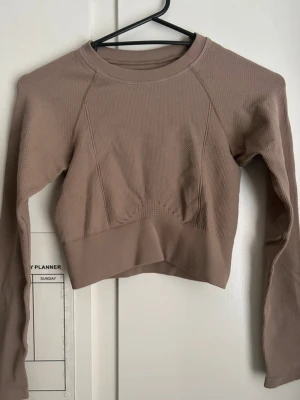 Beige cropped träningströja XS/S - Säljer en beige cropped långärmad träningströja med rund hals och ribbade muddar. Tröjan har en tight passform och är tillverkad i ett stretchigt, strukturerat material som passar perfekt till gymmet eller löpning.   Storlek: XS/S Färg: Brun/ Champagne  Märke: Stadium Skick: Mycket bra – Har aldrig använt