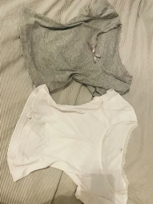 2-pack ribbade spetswear-toppar - Två mysiga ribbade loungewear-toppar, en i ljusgrått med spetskant och liten rosett, och en i vitt med spetsdetaljer vid halsringningen. Båda är kortärmade och har en mjuk, stretchig känsla som passar perfekt för chill dagar hemma.