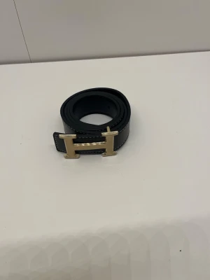 Bälte - Ett svart bälte med guldigt H. Den är helt ny och är 105 cm lång. Pris kan diskuteras och skriv om du har några frågor. 