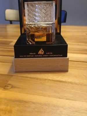 Khamrah Eau de Parfum från Lattafa - Khamrah Eau de Parfum från Lattafa i en lyxig, fyrkantig glasflaska med gulddetaljer. Flaskan rymmer 100 ml och har ett elegant, mönstrat lock. Kommer i en snygg svart och guld förpackning med trädetalj i botten. Perfekt för dig som gillar exklusiva dofter.