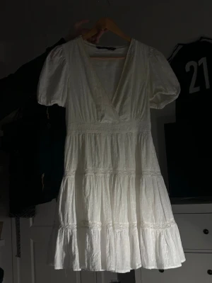 Vit omlottklänning med puffärm - Supersöt vit kortklänning med omlott och v-ringning. Klänningen har puffärmar och volangdetaljer i kjolen. Perfekt för sommarens alla tillfällen!