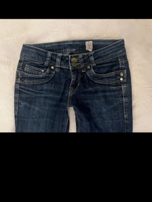 Mörkblå bootcut jeans med låg midja - Snygga mörkblå jeans med bootcut-modell och låg midja. Jeansen har klassiska fickor fram och bak, samt slitna detaljer för en cool look. Bara att skriva om man vill ha mått