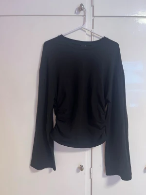 Soft touch långärmad topp med rynk - Säljer en svart långärmad topp med rynkade detaljer i midjan som ger en snygg siluett. Toppen har rund halsringning och är i ett mjukt, stretchigt material. Perfekt att styla med både jeans och kjol.