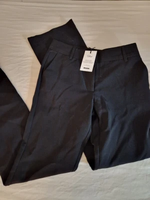 Svarta kostymbyxor PW Sofie - Stilrena svarta kostymbyxor från BikBok PW Sofie med klassisk rak passform och hällor för bälte. Byxorna har diskreta sidofickor och är perfekta för en clean och modern look. Materialet känns mjukt och följsamt, vilket ger en bekväm känsla hela dagen. Byxorna är oanvända med lappen kvar. Hund finns I hemmet. 