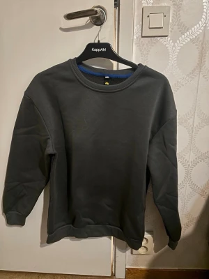 Mörkgrå sweatshirt  - En enkel och stilren mörkgrå sweatshirt som jag köpt i Kosovo. Tröjan har rund halsringning, ribbade muddar vid ärmslut och nederkant samt en avslappnad passform. Perfekt basplagg för en casual look. Använd max tre gånger 