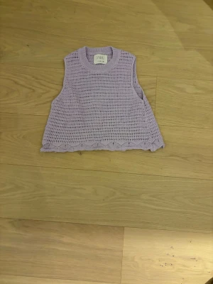 Ljuslila stickad väst från Zara - Säljer en ljuslila stickad väst från Zara i öppen virkad design. Västen har rund halsringning och ribbstickad kant upptill. Perfekt att styla över en t-shirt eller skjorta för en trendig lager-på-lager-look.