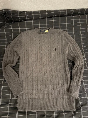 Mörkgrå stickad tröja från Polo Ralph Lauren - Säljer en mörkgrå kabelstickad tröja från Polo Ralph Lauren. Klassisk rund halsringning, långärmad och med den ikoniska broderade loggan på bröstet. Perfekt för kyliga dagar och riktigt snygg till jeans eller chinos. Knappt använd. Är i nyskick, hör av dig om du har några frågor. Kan gå ner till 500 vid snabb affär behöver  få såldt snabbt