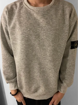 Grå tröja från Stone Island - Snygg grå sweatshirt från Stone Island med klassisk rund hals och ikonisk svart logotyp-patch på vänster ärm. Tröjan har ribbade muddar vid ärmslut och nederkant, perfekt för en clean och avslappnad stil. Tillverkad i mjuk bomullsblandning. Det står storlek M men den är ganska liten i storlek så passar bättre som storlek S. Modellen är 180 och väger 65.