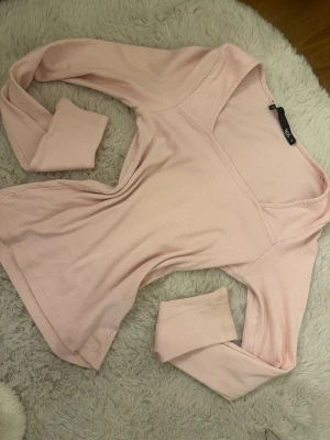 Ljusrosa ribbad långärmad tröja - Supersöt ljusrosa långärmad topp med v-ringning och ribbad struktur. Toppen har en figurnära passform och är tillverkad i mjuk bomullsmix. Perfekt att styla med jeans eller kjol för en trendig look.