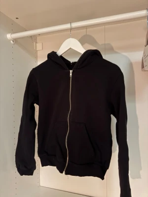 Svart zip hoodie med huva - Klassisk svart zip up hoodie med dragkedja framtill och stor ficka på magen. Hoodien har en skön huva och ribbade muddar vid ärmar och nederkant. Perfekt för en avslappnad och stilren look. Materialet känns mjukt och bekvämt mot huden🤗