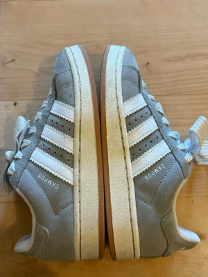Grå adidas Campus sneakers - Snygga grå adidas Campus sneakers med klassiska vita ränder på sidorna och vit sula. Skorna har rund tå, vita snören och gummisula. Använda men fina