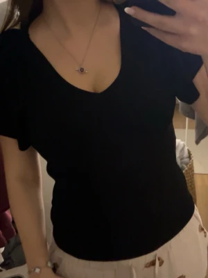 Svart ribbad topp med puffärm och knyt - Svart ribbad topp med puffärmar och v-ringning. Toppen har en snygg knytning i nacken och är tillverkad i ett stretchigt material som sitter snyggt på kroppen. Perfekt för dig som vill ha en enkel men trendig look.