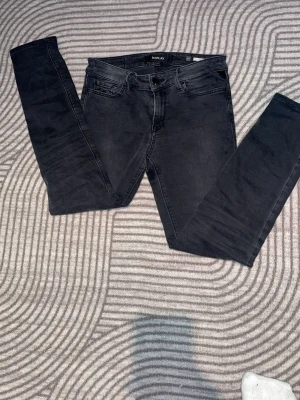 Svarta Replay jeans med stretch - Säljer ett par svarta skinny jeans med smal passform och klassisk femficksdesign. Jeansen har en enkel look utan synliga loggor och är tillverkade i stretchigt denimtyg för extra komfort. Perfekta till en avslappnad stil.