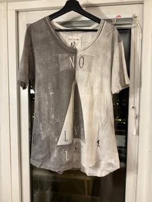 Grå t-shirt från Religion med tryck - Unik t-shirt från Religion i tvättad grå och beige ton med stort grafiskt tryck och texten 'NO LOVE LOST' på framsidan. T-shirten har rund halsringning och korta ärmar. Materialet är mjuk bomull och passformen är loose.