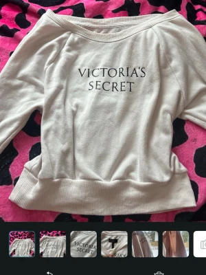 Vit sweatshirt från Victoria's Secret - Säljer en vit/ ljusrosa sweatshirt från Victoria's Secret med svart logotyptryck framtill. Tröjan har bred ribbad mudd i nederkant och vid ärmslut samt en avslappnad passform med båtringad hals. Perfekt för en chill och snygg look. 