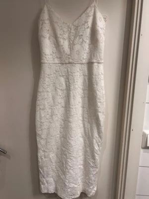 Vit spetsklänning med smala axelband - Säljer en elegant vit klänning med smala axelband och v-ringning. Klänningen har en figurnära passform, passar XS och S! Perfekt för studenten!  Använd max 1 gång.