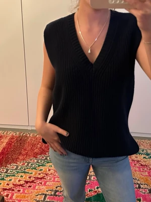 Mörkblå stickad väst med v-ringning - Snygg mörkblå stickad väst med djup v-ringning och bred ribbad kant. Med slits 