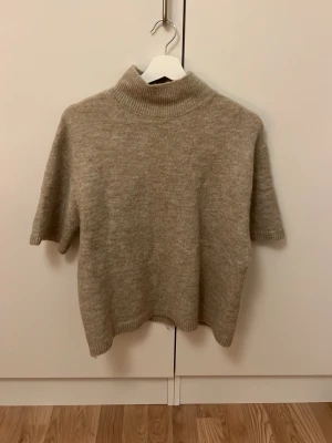 Beige polotröja i ullblandning Gina Tricot - Säljer en beige polotröja från Gina Tricot. Tröjan har korta ärmar och ribbad hög krage som ger en clean och stilren look. Perfekt att styla med jeans eller kjol för en chill vibe.